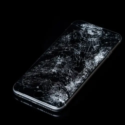 Photograph of an iPhone with a badly shattered screen with a black background.