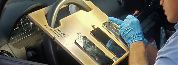 Photo of a technician inside their car, replacing a broken iPhone screen in the customer's driveway.